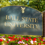 A "Ball State University" sign is surrounded by flowers and trees