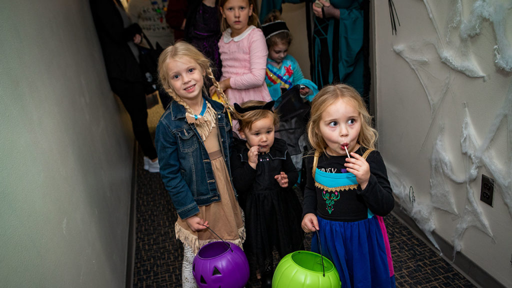 Children trick or treating while eating suckers.