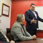 Haris in a business suit talking and gesturing in front of a whiteboard