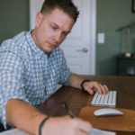 Josh seated at a computer workstation in a home office while writing