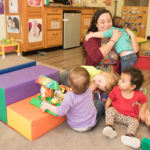 Michelle smiling and lifting a young child while other children play