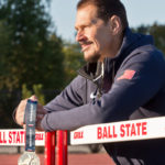 Larry holding medal while leaning on a hurdle