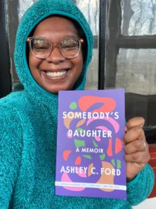 black woman in a teal hoodie holding a book